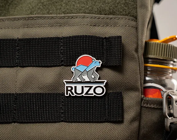 A RUZO bear custom logo enamel pin attached to an olive green tactical backpack