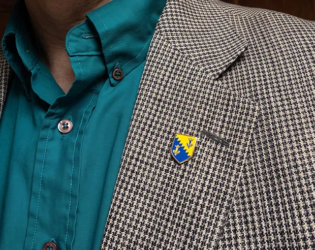 A small blue and yellow shield custom pin on a houndstooth blazer lapel