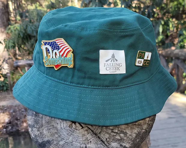 “Do Something” enamel pin and PACC enamel pin pinned to a green bucket hat