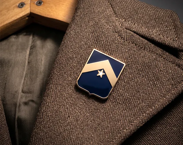 A shield-shaped navy blue enamel gold pin on a brown tweed coat lapel