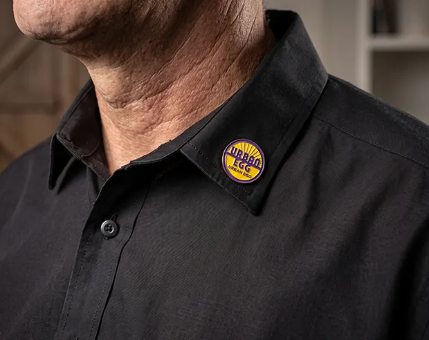 A custom Urban Egg round enamel pin on a black shirt collar