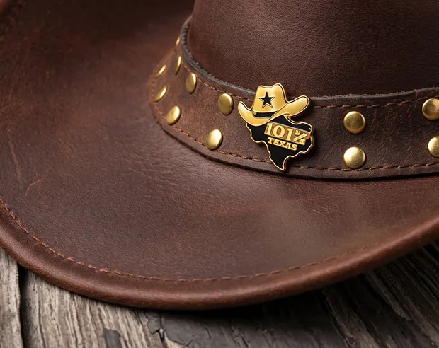 A Texas-shaped 101 gold-plated enamel pin on a brown leather cowboy hat