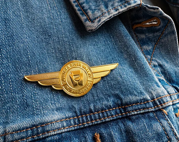 A gold aviator wing die stuck pin on a blue denim jacket