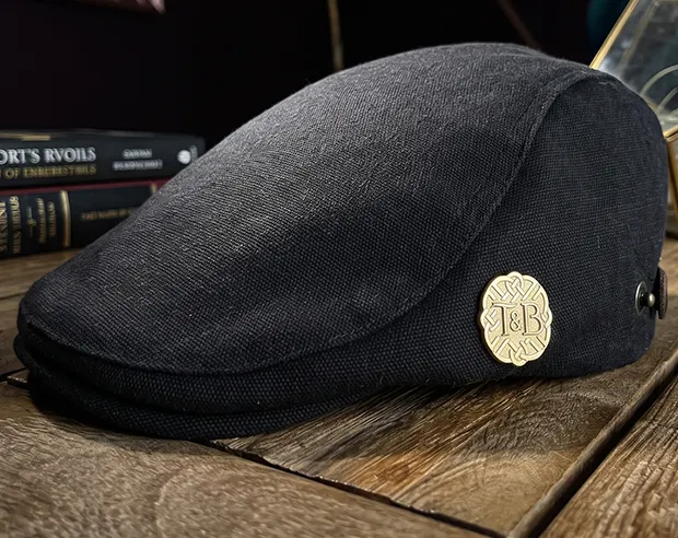 A gold plated round "T&B" monogram pin on a black flat cap