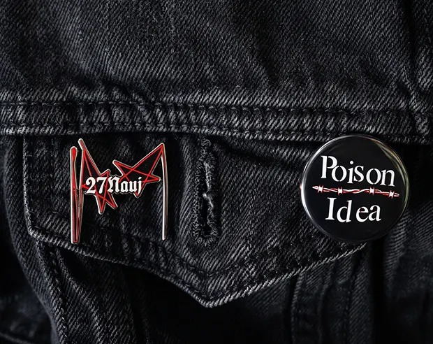 A custom punk enamel pin and a "Poison Idea" button badge on a black denim jacket pocket