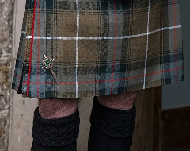 An antique silver sword pin with green shamrock on a tartan kilt