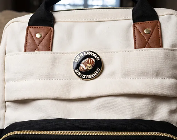 A round football-themed enamel pin on a canvas laptop bag pocket