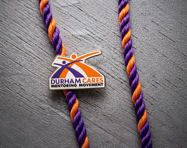 A "Durham Cares Mentoring Movement" pin attached to a purple and orange twisted lanyard