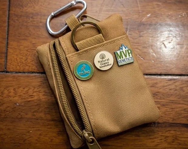 Three custom enamel pins pinned on a khaki tactical pouch wallet