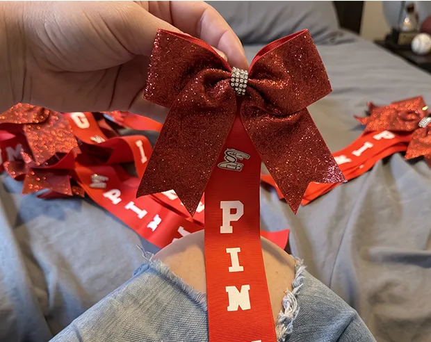 A custom enamel pin attached to a red glitter cheer bow ribbon