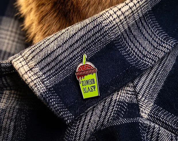A "Zombie Blast" bubble tea cup design hard enamel pin on the collar of a shirt