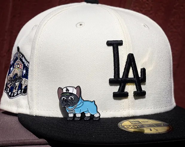 A cute French bulldog wearing an LA cap enamel pin on a white fitted baseball hat