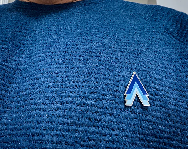 A blue chevron-shaped logo gradient printed pin on a textured sweater