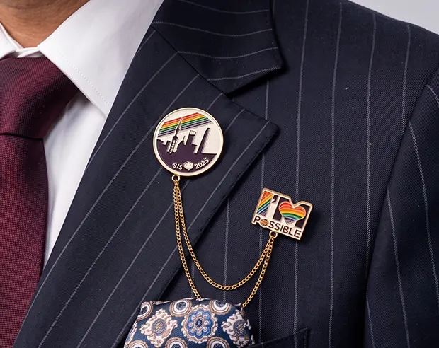 A rainbow-themed chained enamel tuxedo pin on a navy pinstripe suit